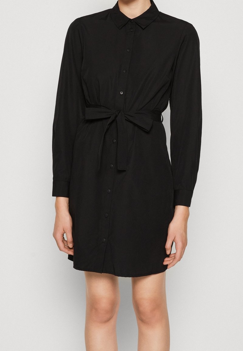 Robe noire à boutonnière avec manches longues, détail de ceinture à nouer et col. Tissu lisse, longueur mi-cuisse, léger éclat.