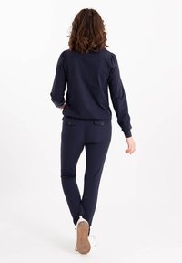 Navyblauwe trainingsbroek met een aansluitend ontwerp. Het bovenstuk heeft poffende mouwen, terwijl de broek twee achterzakken heeft. Gemaakt met witte sneakers.