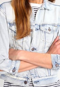 Light wash denim jacket with button closures, flap pockets, and rolled up sleeves. Features a classic collar and a relaxed fit.