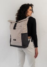 Zaino a roll-top in grigio chiaro e nero, realizzato in tessuto resistente, dotato di tasca frontale, spallacci regolabili e design minimalista.