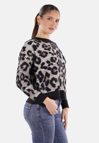 Maglione leopardato in morbido tessuto, con collo tondo, polsini e orlo a coste neri, e vestibilità comoda. Abbinato a jeans blu aderenti.