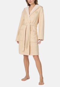 Beżowy szlafrok frotte z kapturem, wyposażony w kołnierz szalowy, dwie przednie kieszenie, pasek i logo na piersi. Miękka faktura.