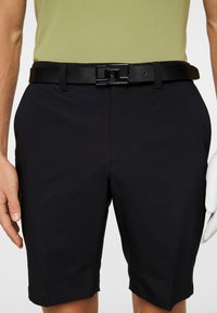 Czarne szorty o gładkiej fakturze, z płaskim przodem i bocznymi kieszeniami. W połączeniu z czarnym paskiem i jasnym koszulą.