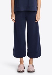 Pantaloni a gamba larga in navy in tessuto morbido con una texture liscia, con una leggera svasatura all'orlo sopra zoccoli rosa con dettagli chiodati.