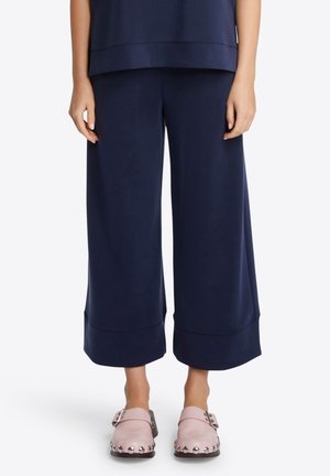 Pantalons larges navy en tissu doux avec une texture lisse, présentant un léger évasement à l'ourlet au-dessus de sabots roses avec des accents cloutés.
