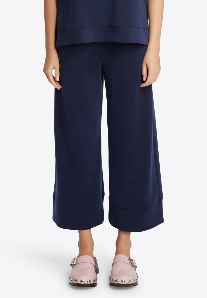 Pantaloni a gamba larga in navy in tessuto morbido con una texture liscia, con una leggera svasatura all'orlo sopra zoccoli rosa con dettagli chiodati.