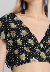 Top corto nero con motivo a pois e ricami floreali, design a V e maniche arricciate.