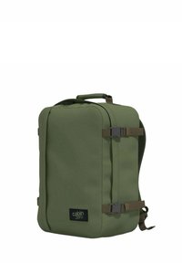 Vihreä kankainen reppu, jossa on suorakulmainen muoto, kiinteä kahva, säädettävät hihnat ja sivun solkilukko. Yksinkertainen logo edessä.