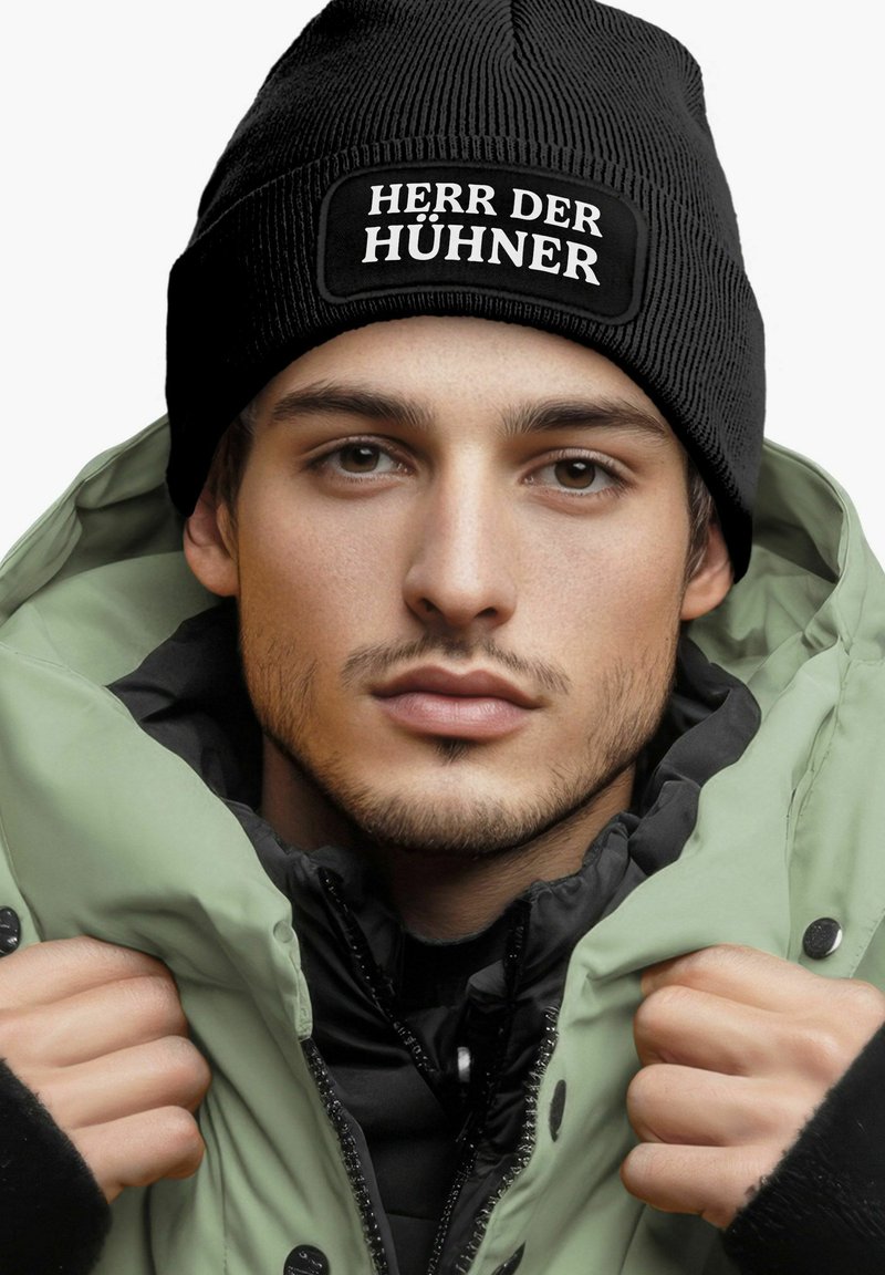 Black ribbed beanie with "HERR DER HÜHNER" patch, worn with a black and light green puffer jacket featuring a high collar and snap fasteners.