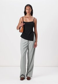 Top nero senza maniche con orlo asimmetrico, abbinato a pantaloni a gamba larga grigio chiaro a righe e scarpe a motivi marroni. Tiene una borsa a spalla marrone.