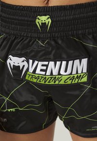 Black training shorts featuring green accents and lines, a VENUM logo at the waistband, and a prominent "TRAINING CAMP" patch.