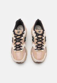 Light pink and beige running shoes with black laces, textured upper, green accents, and cushioned sole. Features reflective logo and stitching.