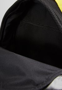 Interior de mochila negra con forro de tela suave, que presenta un bolsillo con cremallera en un lado y una parte superior de malla para ventilación.