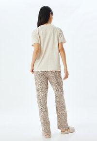 Lichtbeige t-shirt met korte mouwen, gecombineerd met crèmekleurige en bruin gestreepte pyjamabroek. Zachte textuur, relaxte pasvorm, en instap pantoffels.