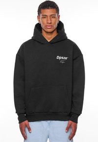 Svart hettegenser med frontlomme, hette og ribbede mansjetter. Har hvit "Dpsze"-logo på brystet. Myk stoff, avslappet passform.
