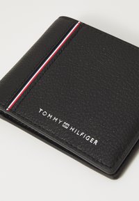 Schwarze Lederbörse mit strukturiertem Finish, ausgestattet mit einem rot-weiß-blauen Streifen und geprägtem "TOMMY HILFIGER"-Logo.