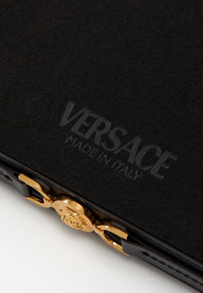 Artículo de cuero negro con el logo en relieve "VERSACE MADE IN ITALY", que presenta un cierre de hardware dorado con un emblema detallado.