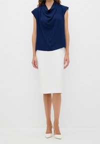 Top navy blu a maniche corte con scollatura drappeggiata e motivo testurizzato, abbinato a una gonna a matita bianca fino al ginocchio e a delle decolleté bianche a punta.