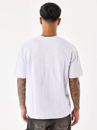 Camiseta corta de manga corta en color púrpura claro con un diseño de corazón bordado que presenta un mapa mundi y texto en la parte posterior. Textura suave y corte relajado.