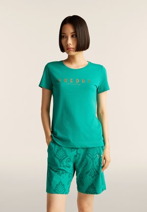 T-shirt in cotone turchese con logo "FREDDY", abbinato a pantaloncini coordinati con un motivo decorativo. I pantaloncini hanno una vestibilità comoda.
