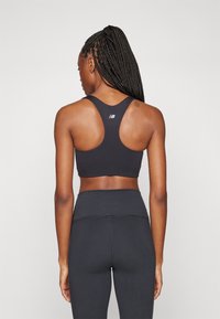 Sostén deportivo negro con diseño de espalda de nadador, hecho de una tela suave. Logo de New Balance en la parte superior de la espalda. Combinado con leggings negros de tiro alto.
