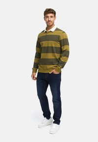 Zielono-żółty pasiasty longsleeve polo z białym kołnierzykiem, w połączeniu z ciemnoniebieskimi dżinsami i białymi trampkami.