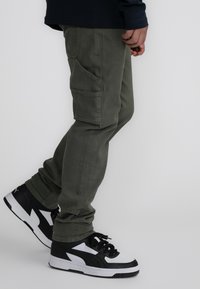 Groene cargobroek met zijzakken, gemaakt van zachte stof. Gecombineerd met zwart-witte sneakers met een low-top ontwerp en veters.