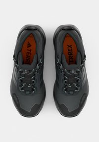 Par sorte og grå sportssko med mønstrede snørebånd og orange indlægssåler mærket Terrex, set oppefra.