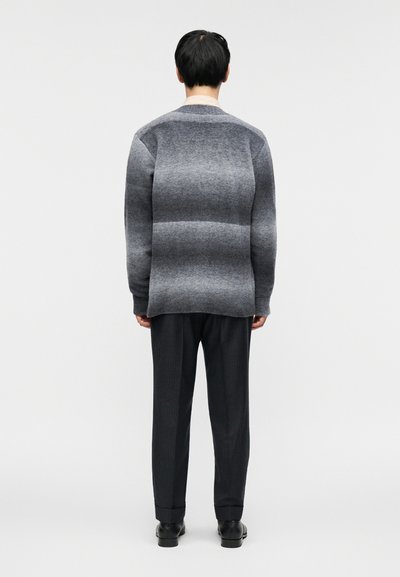 Γκρι πλεκτό πουλόβερ με διάφορες αποχρώσεις, σε χαλαρή εφαρμογή και στρογγυλή λαιμόκοψη. Συνδυασμένο με σκούρα ριγέ παντελόνια και μαύρα παπούτσια.