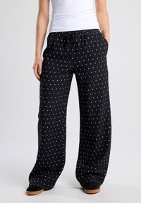 Black wide-leg trousers featuring a drawstring waist and white polka dots. Made from lightweight fabric with side pockets.