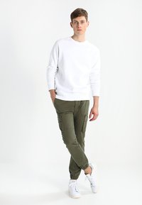 Witte sweatshirts met ronde hals, olijfgroene cargobroeken met zijzakken en witte sneakers. Casual fit met elastische manchetten op de broeken.