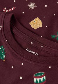 Burgunderfarget bomull T-skjorte med festlige mønstre: trær, snøfnugg, godterstenger, gaver og en tromme. Ribbete halslinning med merke.