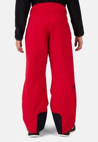 Pantaloni da neve rossi con una vestibilità ampia e comoda. Realizzati in materiale durevole, presentano dettagli neri nella parte inferiore e una patche con logo sul lato.
