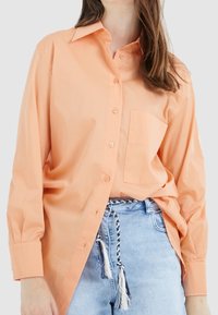 Chemise à manches longues, boutonnée, en pêche clair, avec un col classique, une poche poitrine et une coupe décontractée. Fabriquée en tissu de coton.