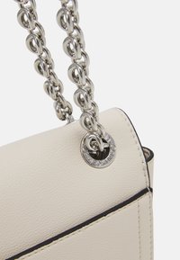 Světle béžová kožená kabelka s stříbrným řetízkem, kulatým kovovým detailem a kontrastním námořnickým prošíváním podél okrajů.