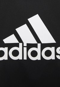 Černá tkanina s výrazným bílým logem Adidas a třemi pruhy nad názvem značky. Hladká textura, minimalistický design.