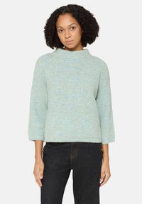 Jasnoniebieski, teksturowany sweter dziany z wysokim kołnierzem i rękawami do łokci, zestawiony z ciemnymi dżinsami.