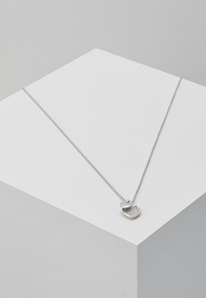 Collier délicat en argent avec deux pendentifs en forme de cœur, l'un uni et l'autre incrusté de petits cristaux, présenté sur un bloc géométrique blanc.
