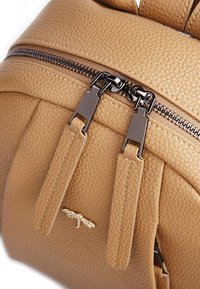 Zaino in pelle marrone chiaro con superficie texture, doppie cerniere metalliche, spallacci sottili e un piccolo dettaglio in oro a forma di libellula.