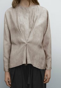 Haut à manches longues beige avec un col en V et une couture centrale. Tissu doux et texturé avec une coupe décontractée, porté avec une jupe noire.