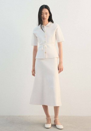 Top blanco de manga corta con cuello y cierre de botones, combinado con una falda larga a juego. Textura suave y lisa con detalle de cinturón anudado.