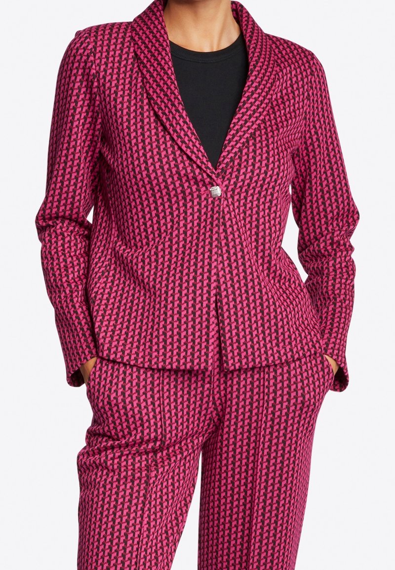 Roze en zwart patroonblazer met ingestikte kraag, enkele knoopsluiting en vrouwelijke pasvorm. Gekleed met bijpassende broek, beide met textuur.