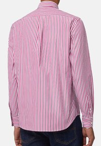 Lange mouwen shirt in roze en witte gestreepte katoen, met een knoopkraag en afgeronde onderkant. Achteraanzicht toont een getailleerde pasvorm en manchetdetails.