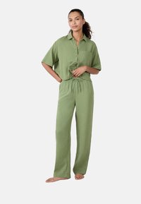 Conjunto de loungewear con textura arrugada en color verde, que incluye una camisa de botón de manga corta con bolsillo y pantalones de cintura elástica. Ajuste suave y relajado.