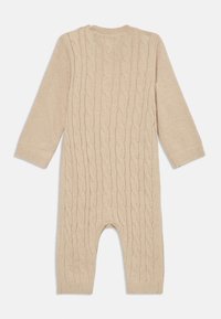 Une combinaison en tricot beige avec un motif en tricot torsadé, des manches longues, un col rond et une zone de pieds ouverte. Texture douce, poignets et ourlet côtelés.