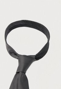 Fekete nyakkendő sima selyemfényű és texturált anyagból készült szalaggal. Klasszikus hurkos kialakítással és központi csomóval.