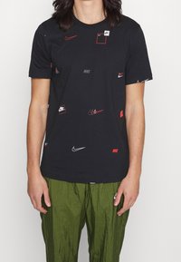 Camiseta de algodón negra con varios logotipos de Nike en blanco y rojo, de manga corta, cuello redondo, corte holgado y textura suave.