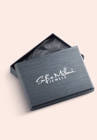 Grå tekstureret smykkeboks med en lågklap. toppen har logoet "Sofia Milani JEWELS" i hvid. Indvendigt foret med sort silkepapir.