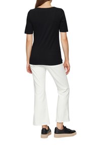 Black short-sleeve t-shirt, plain design, paired with white wide-leg pants. Black sneakers with a textured beige sole. Rear view detail.