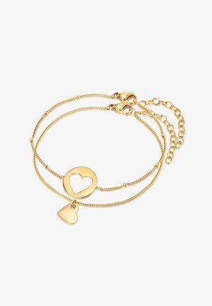 Pulsera en tono dorado con dos cadenas, que presenta un charm en forma de corazón y un centro en forma de corazón abierto. Texturizada, con cierre de langosta y cadena ajustable.